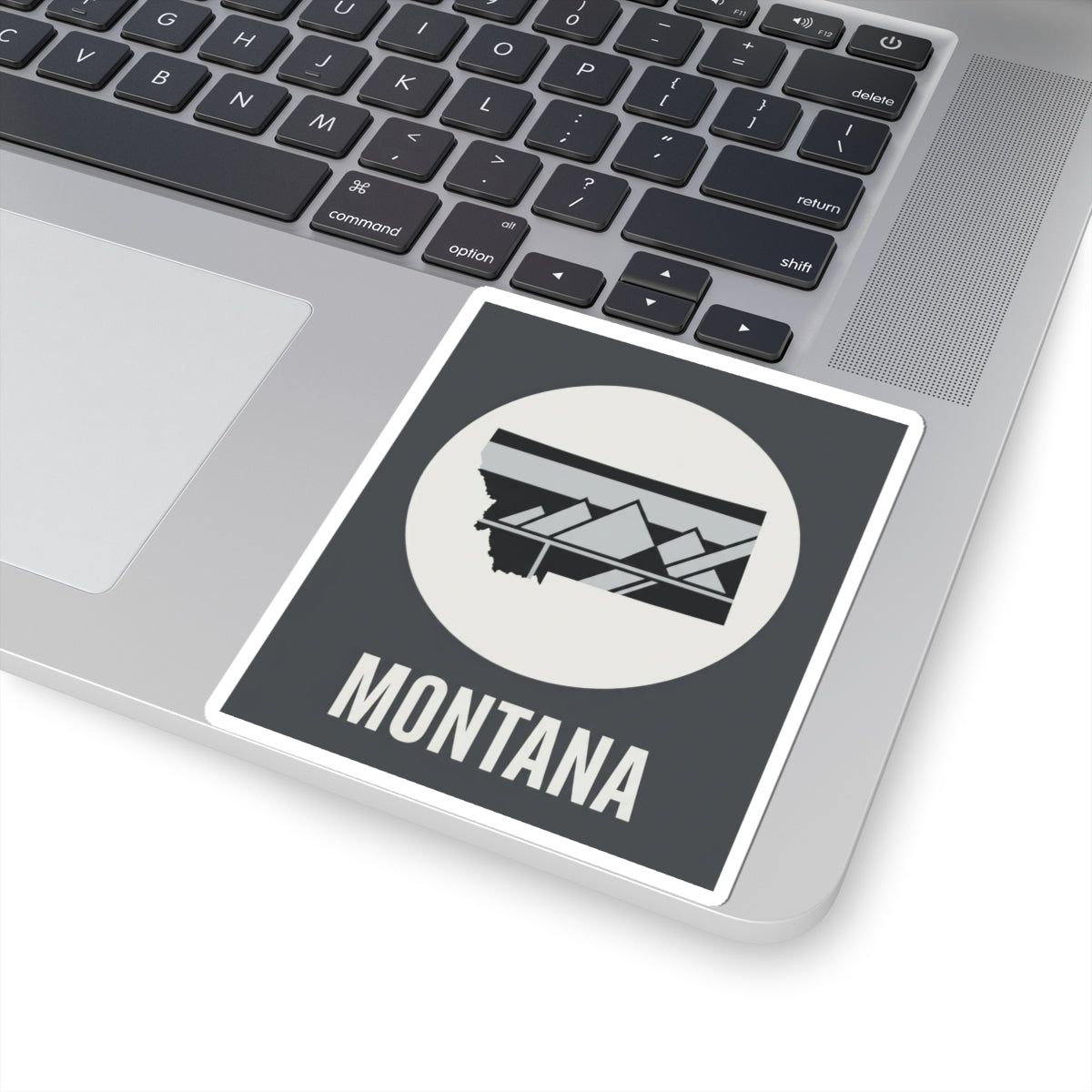 Montana mountain badge sticker on laptop screen, white circle emblem with landscape graphic and MONTANA