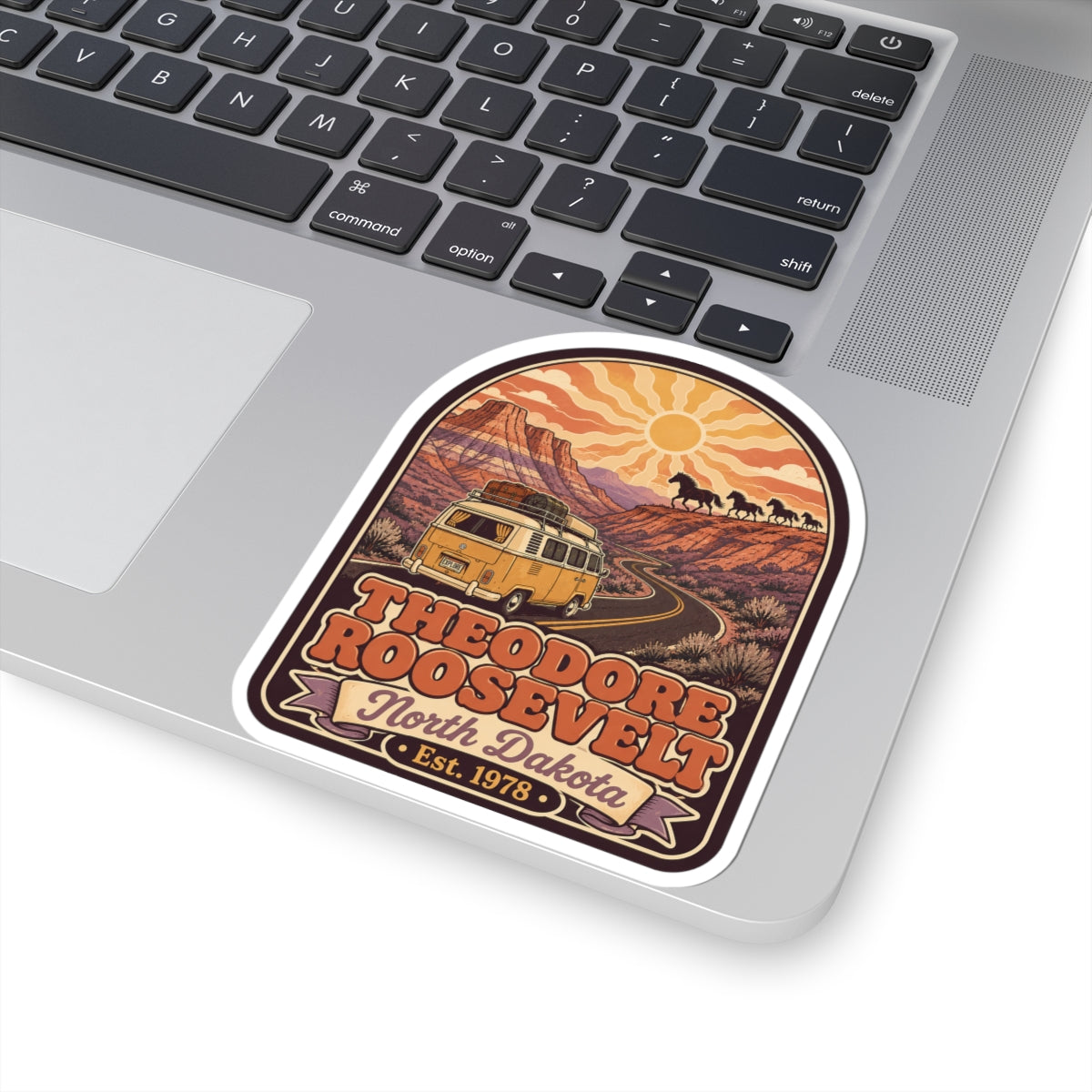 Kiss-cut sticker on laptop lid, desert road scene with horses and Theodore Roosevelt lettering