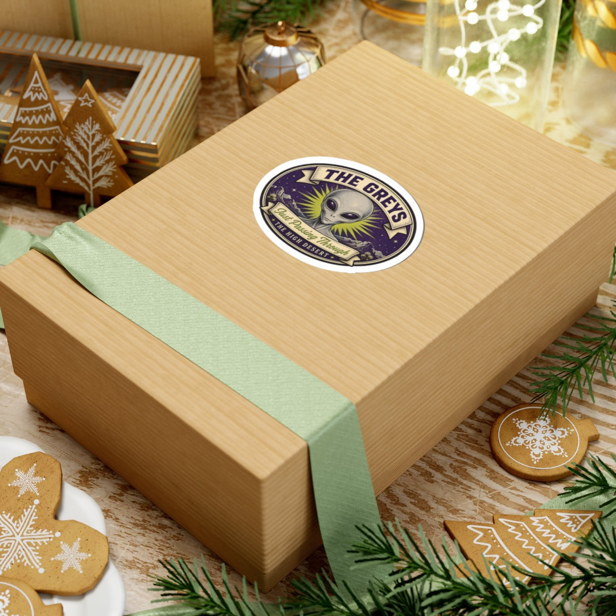 Circular alien head sticker on a wrapped gift box with a mint ribbon and “THE GREYS”