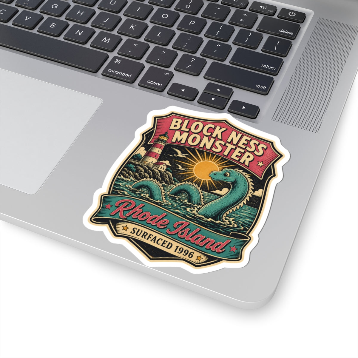 Shield-shaped vinyl sticker showing teal monster, sun over waves, and 'Rhode Island' ribbon.