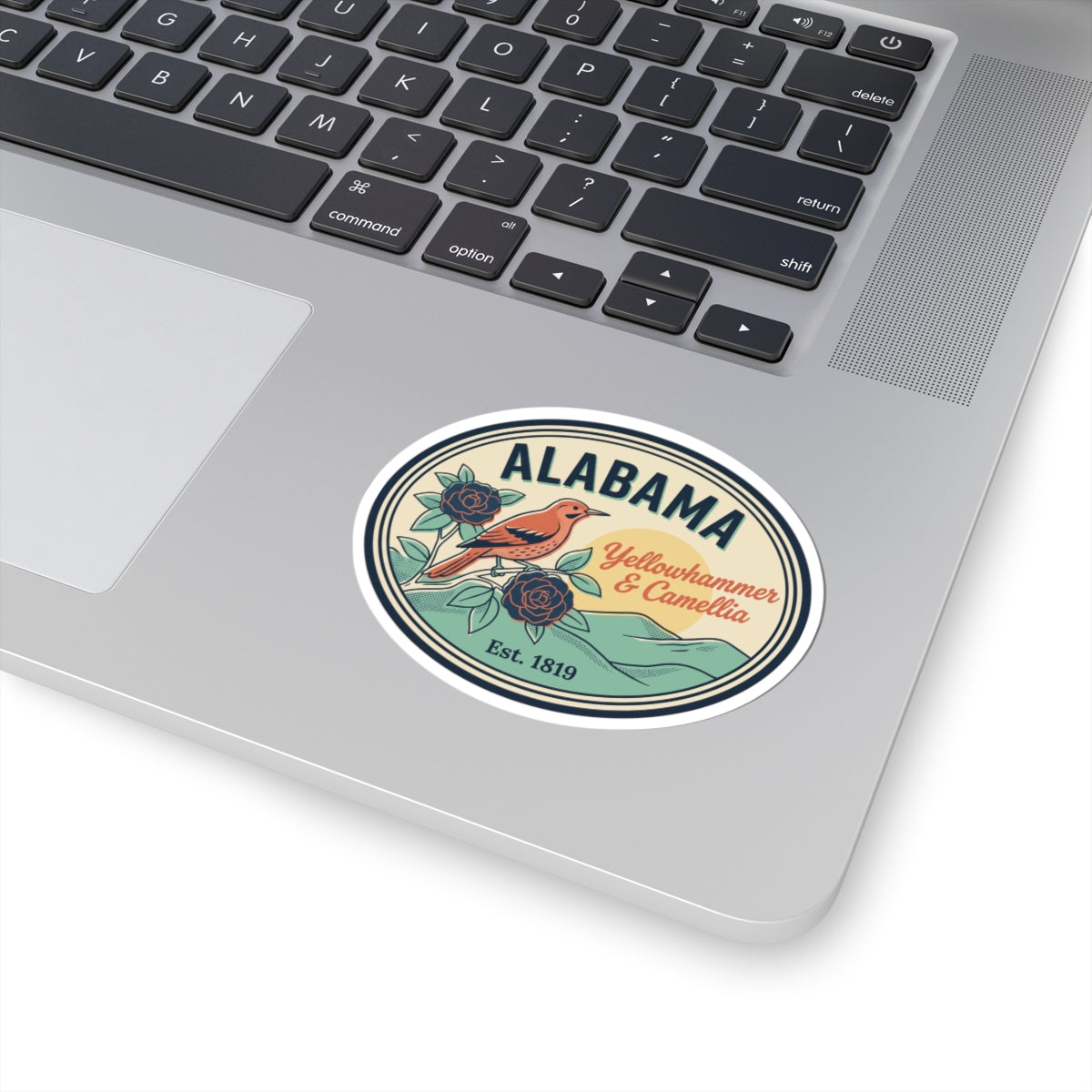 Alabama oval vinyl sticker on silver laptop lid, bird-and-rose state badge design