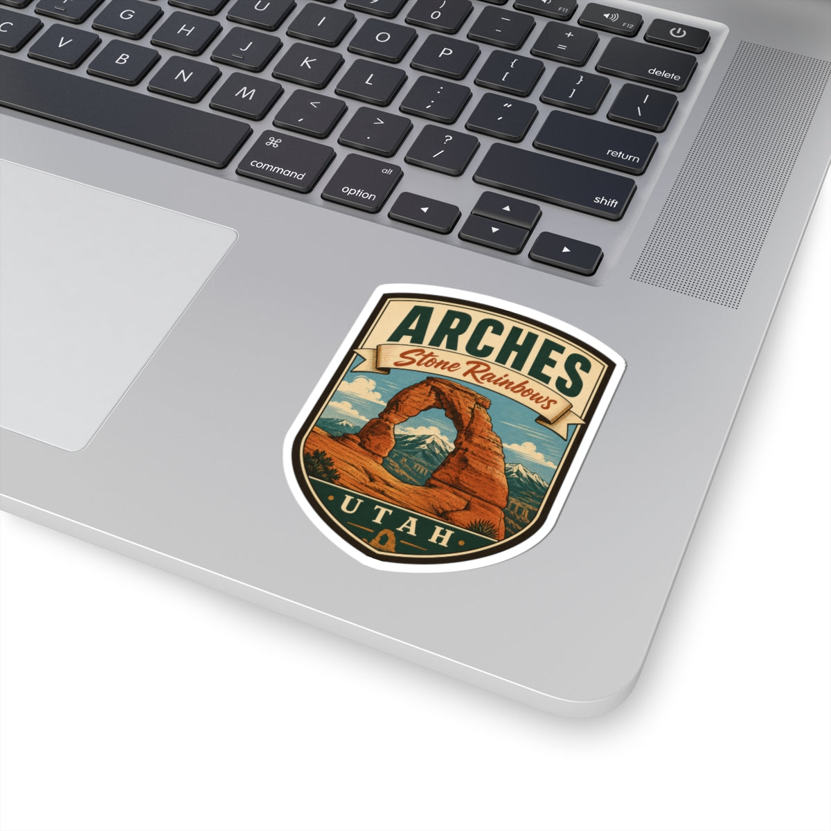 Shield-shaped Arches Utah kiss-cut sticker with Delicate Arch and Stone Rainbows banner, angled