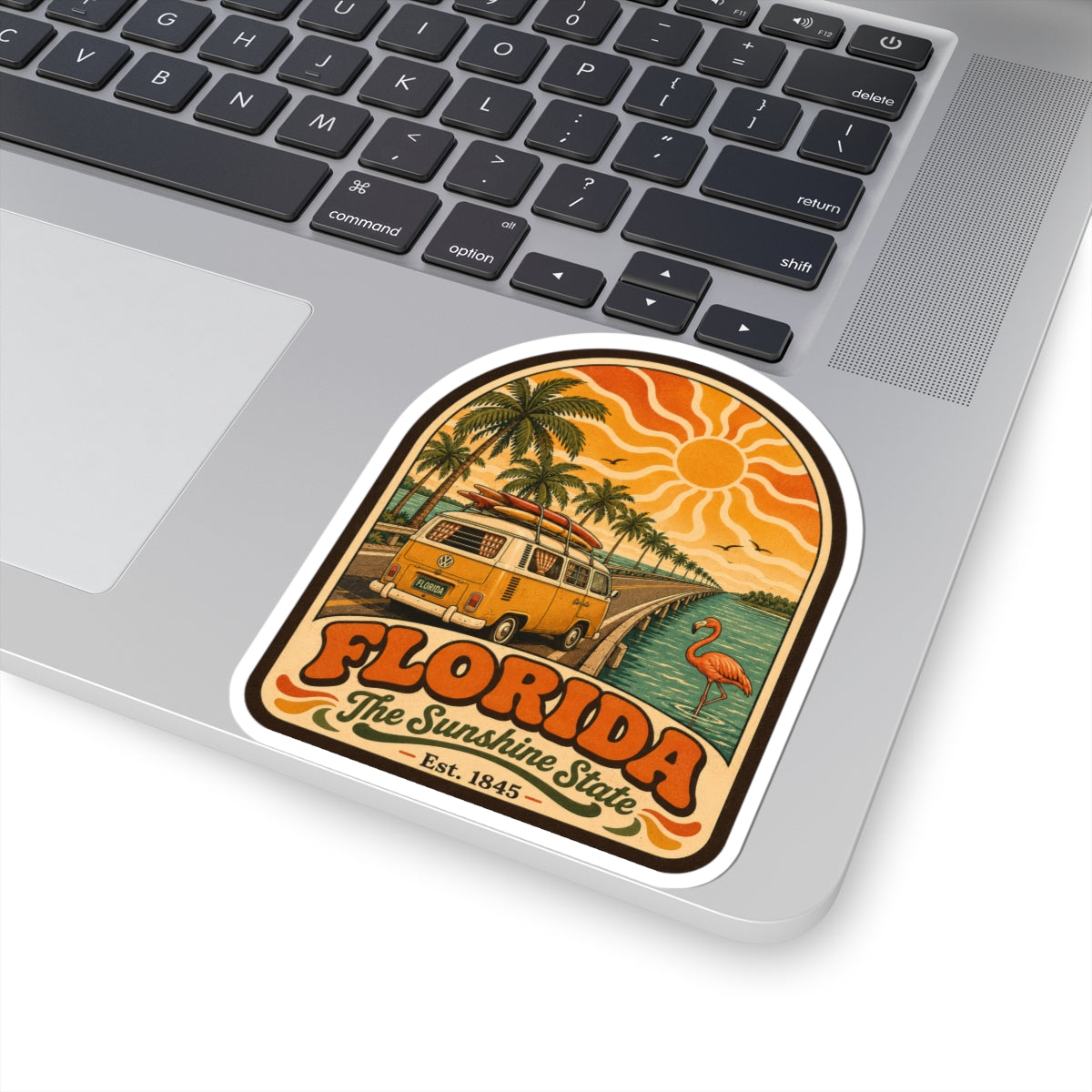Florida retro sticker on laptop, showing surf bus, palm trees, sun, and flamingo