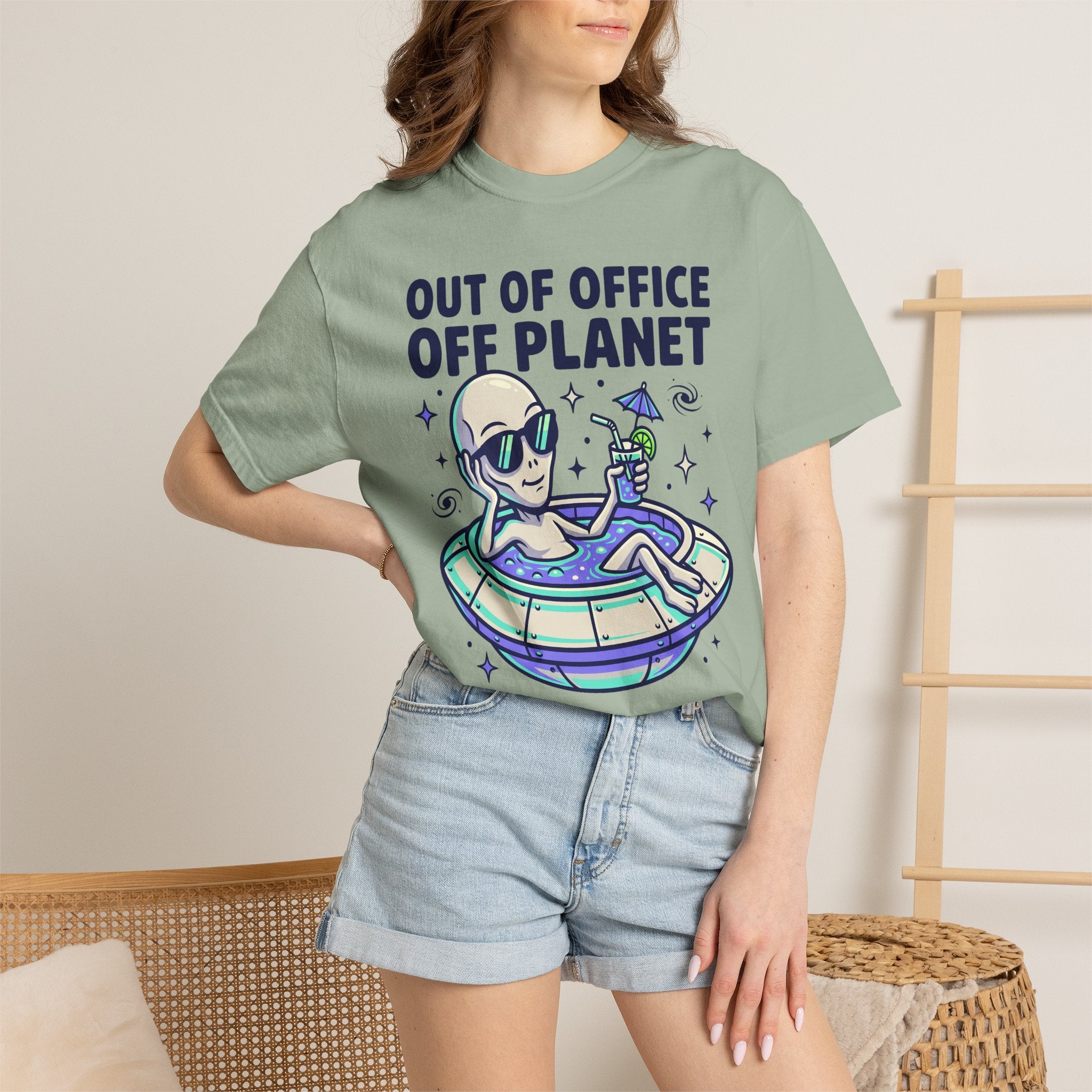 Sage green T-shirt worn by model, alien floatie graphic with 'OUT OF OFFICE OFF PLANET'