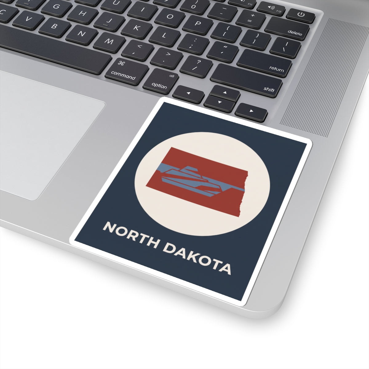 North Dakota map sticker on a laptop, navy square with cream circle and red map icon