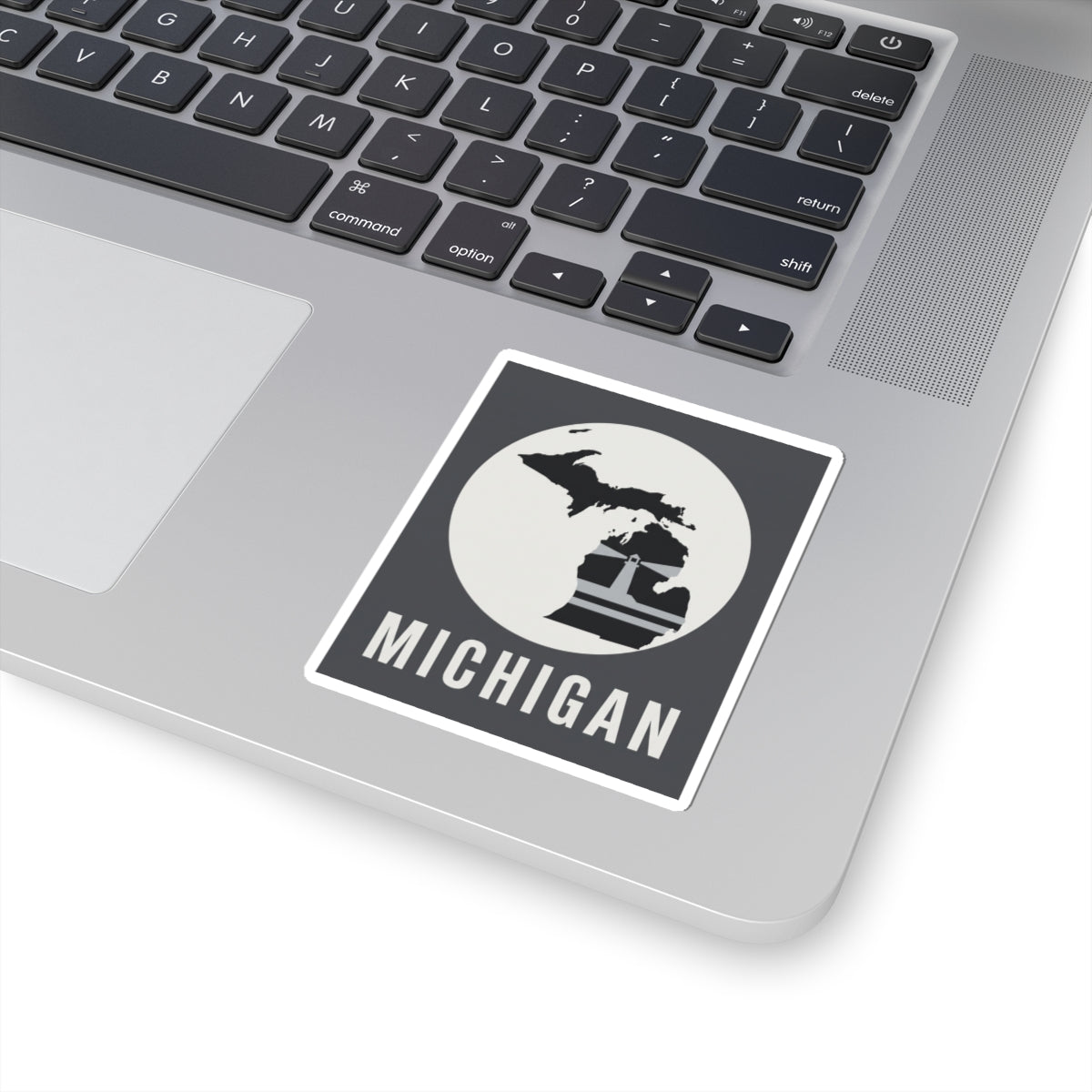 Small square Michigan sticker on a laptop trackpad, showing map silhouette and “MICHIGAN”.