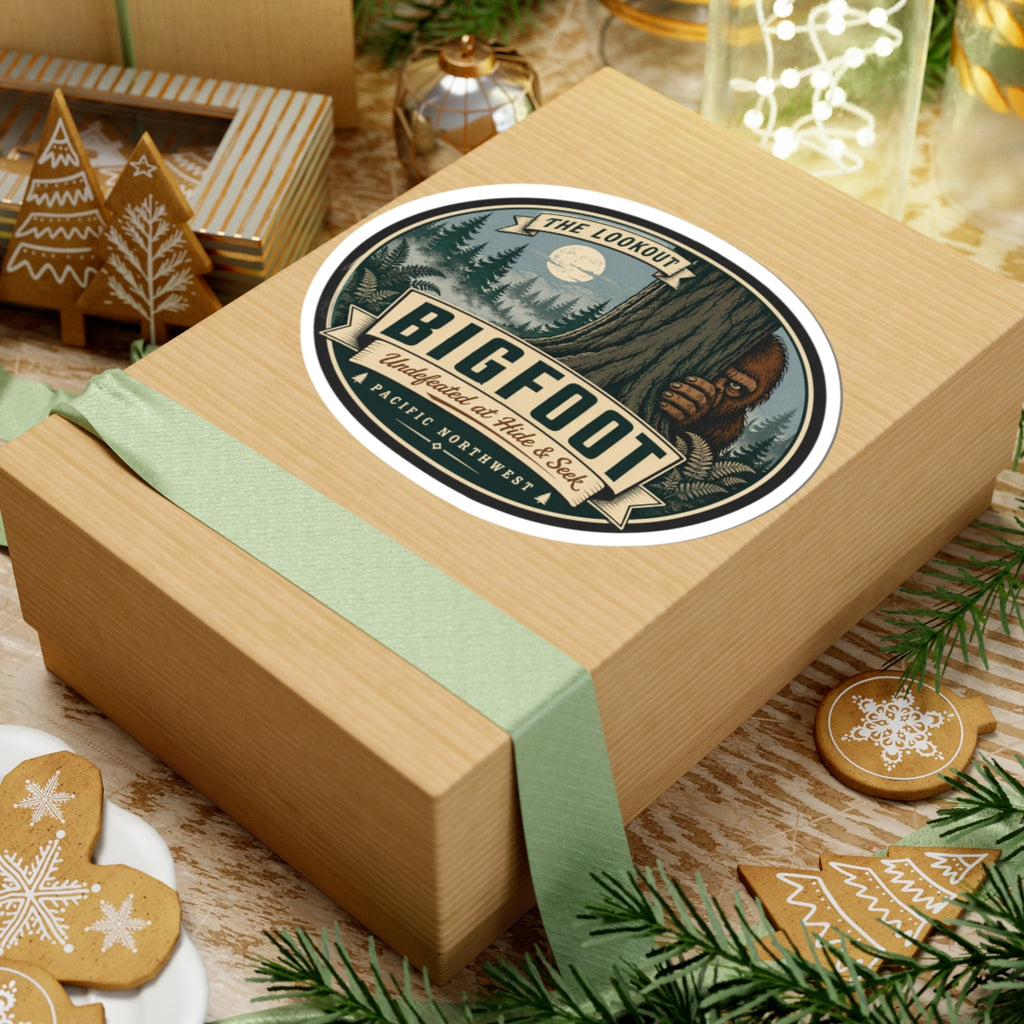 Round kiss-cut Bigfoot outdoor logo vinyl sticker on tan gift box near greenery