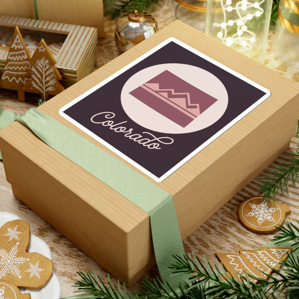 Colorado sticker on a wrapped gift: dark purple square with mauve landscape and “Colorado”