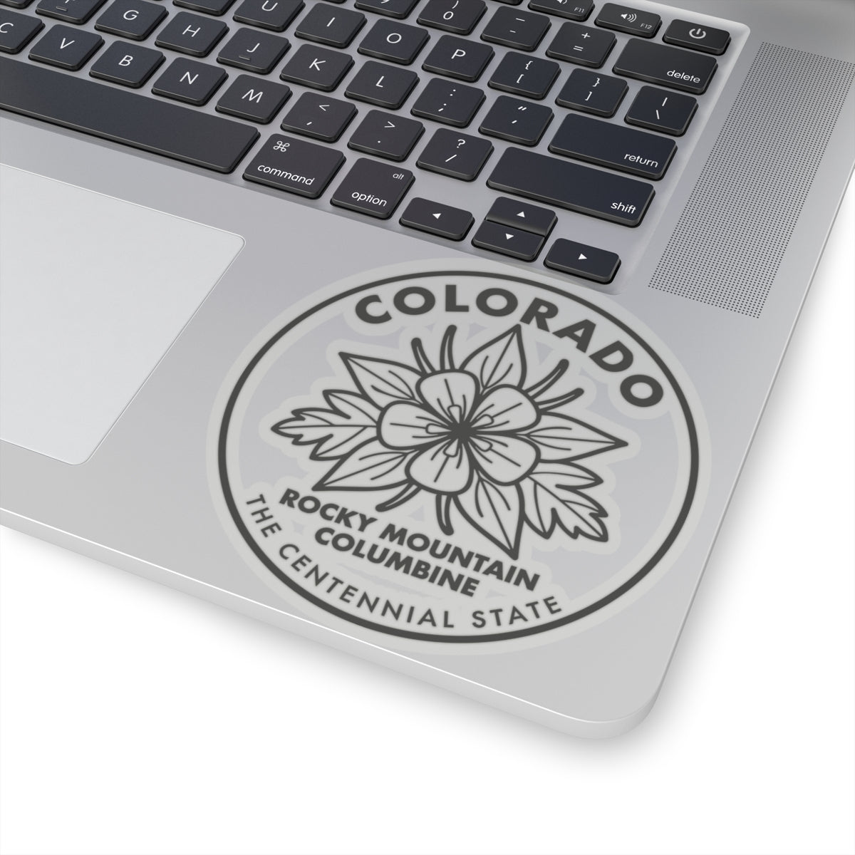 Laptop sticker close-up: round Colorado columbine seal with “ROCKY MOUNTAIN” text