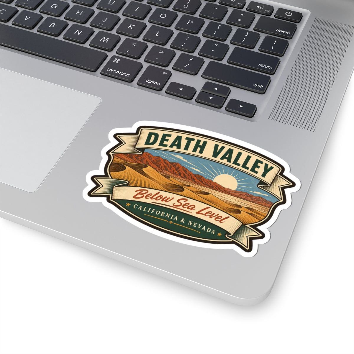 Die-cut sticker showing desert dunes, mountains, sun rays, “Death Valley” and “Below Sea Level”