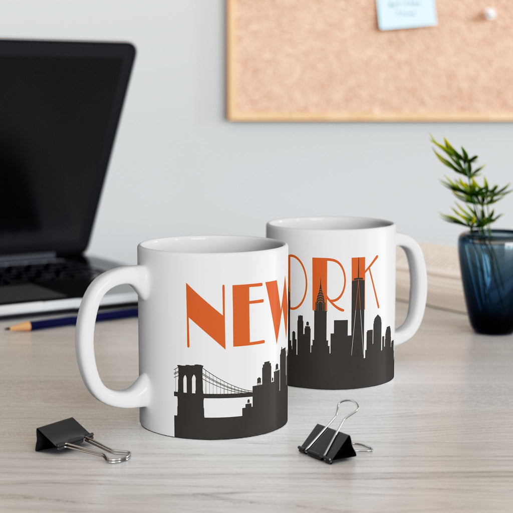 Two white ceramic mugs with orange “NEW” text and black skyline design