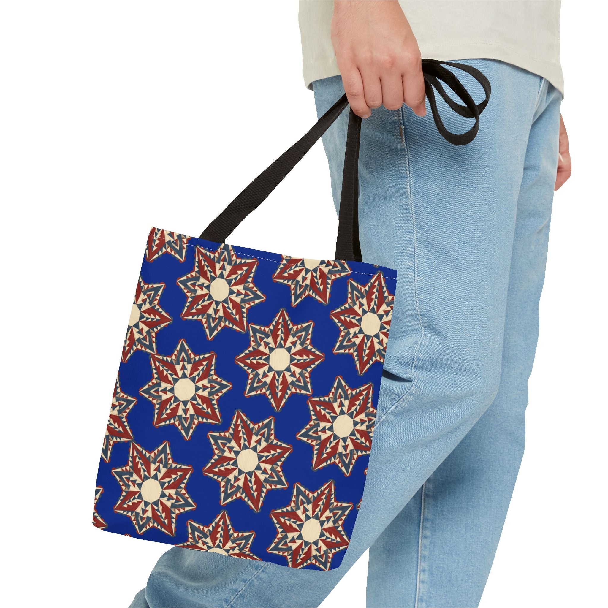 Blue tote bag with starburst floral mandala pattern and black handles, held in hand