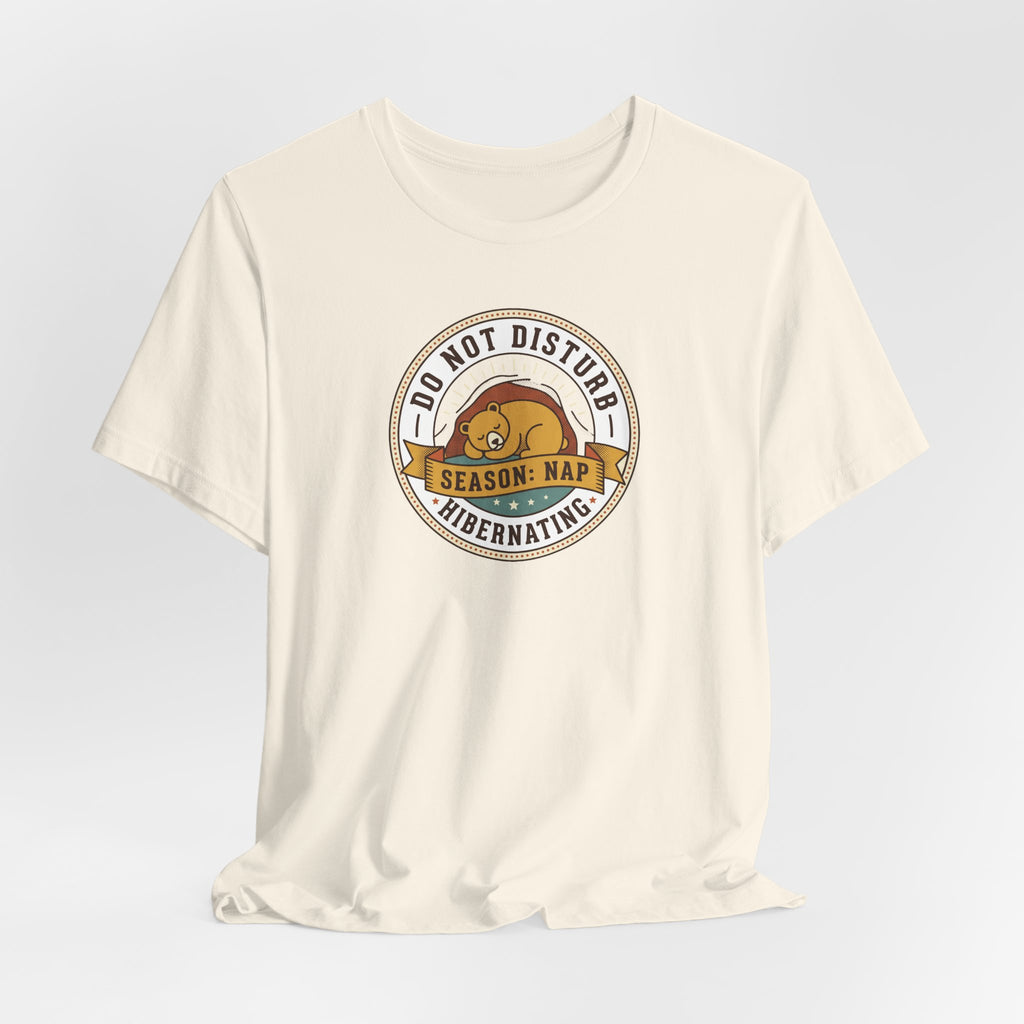 Cream T-shirt with round bear sleeping badge graphic at center chest