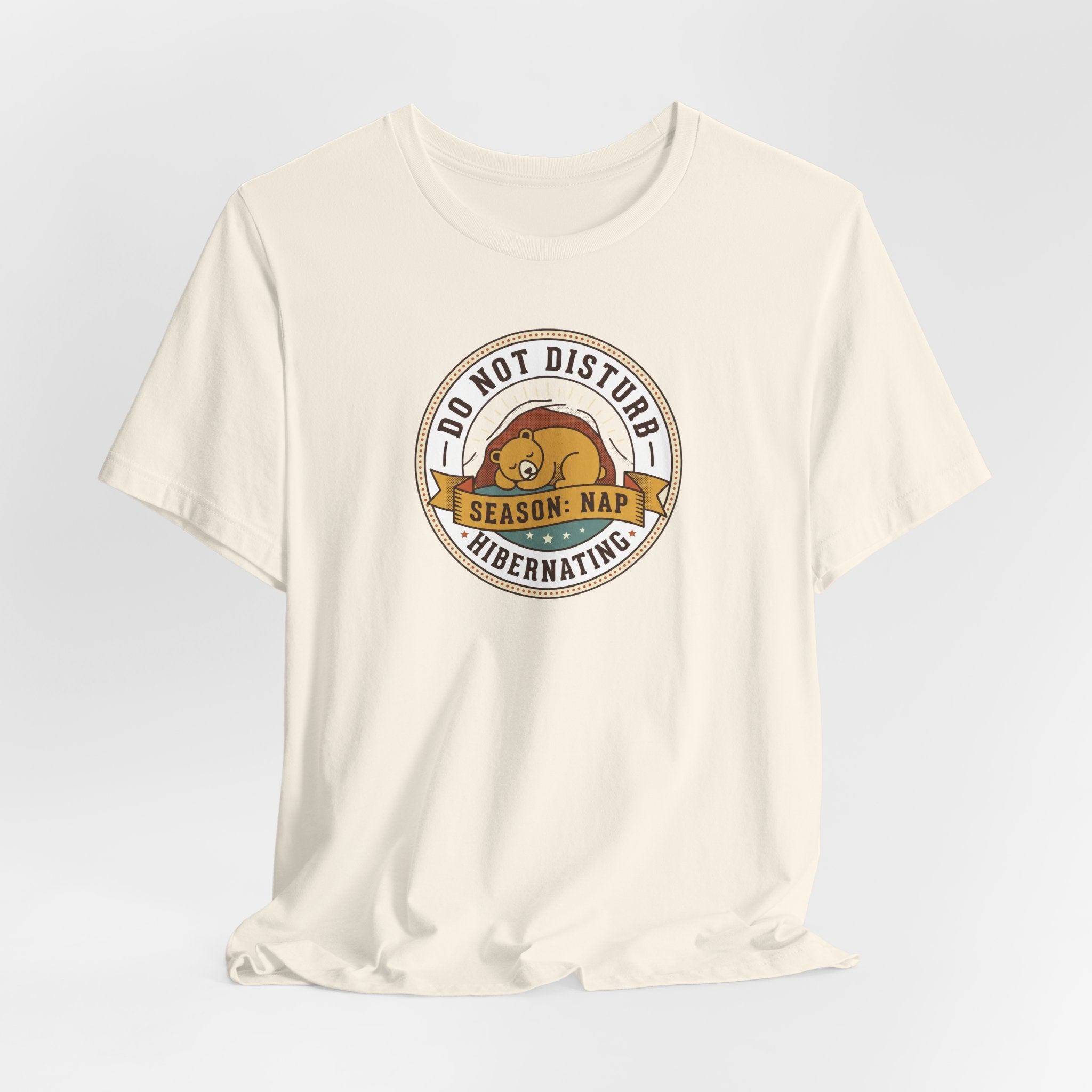 Cream T-shirt with round bear sleeping badge graphic at center chest