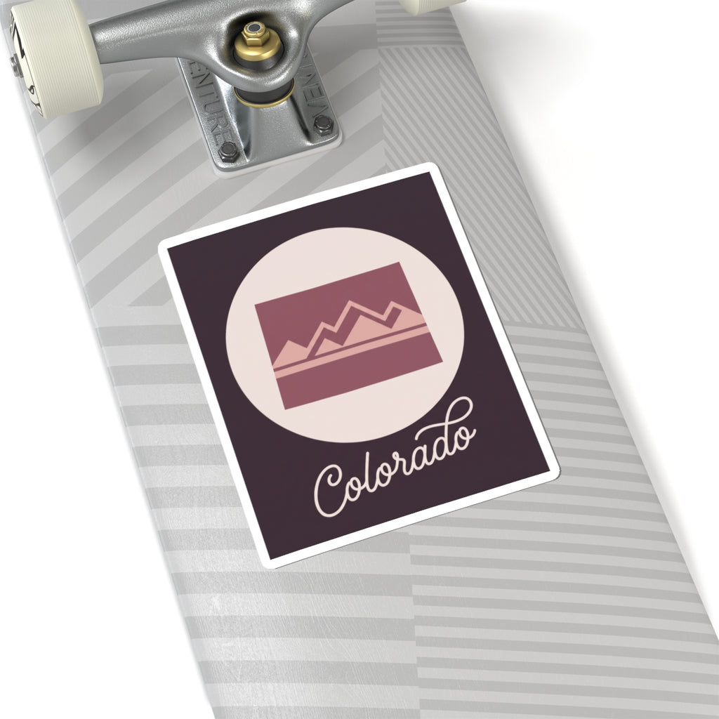 Colorado sticker on a roller suitcase, dark square with mauve landscape icon and “Colorado”