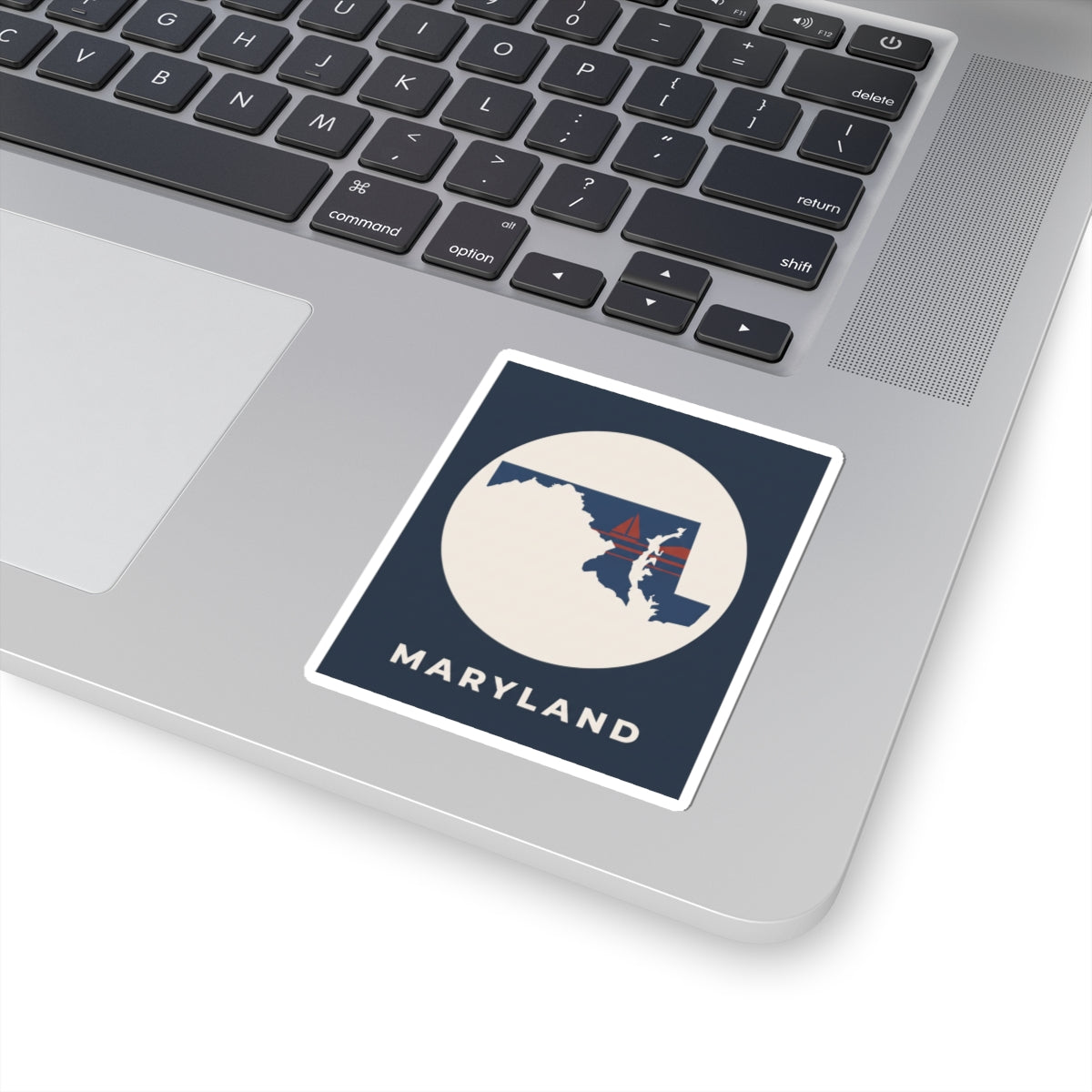 Maryland map sticker on a laptop keyboard, navy square with circular state and sailboat
