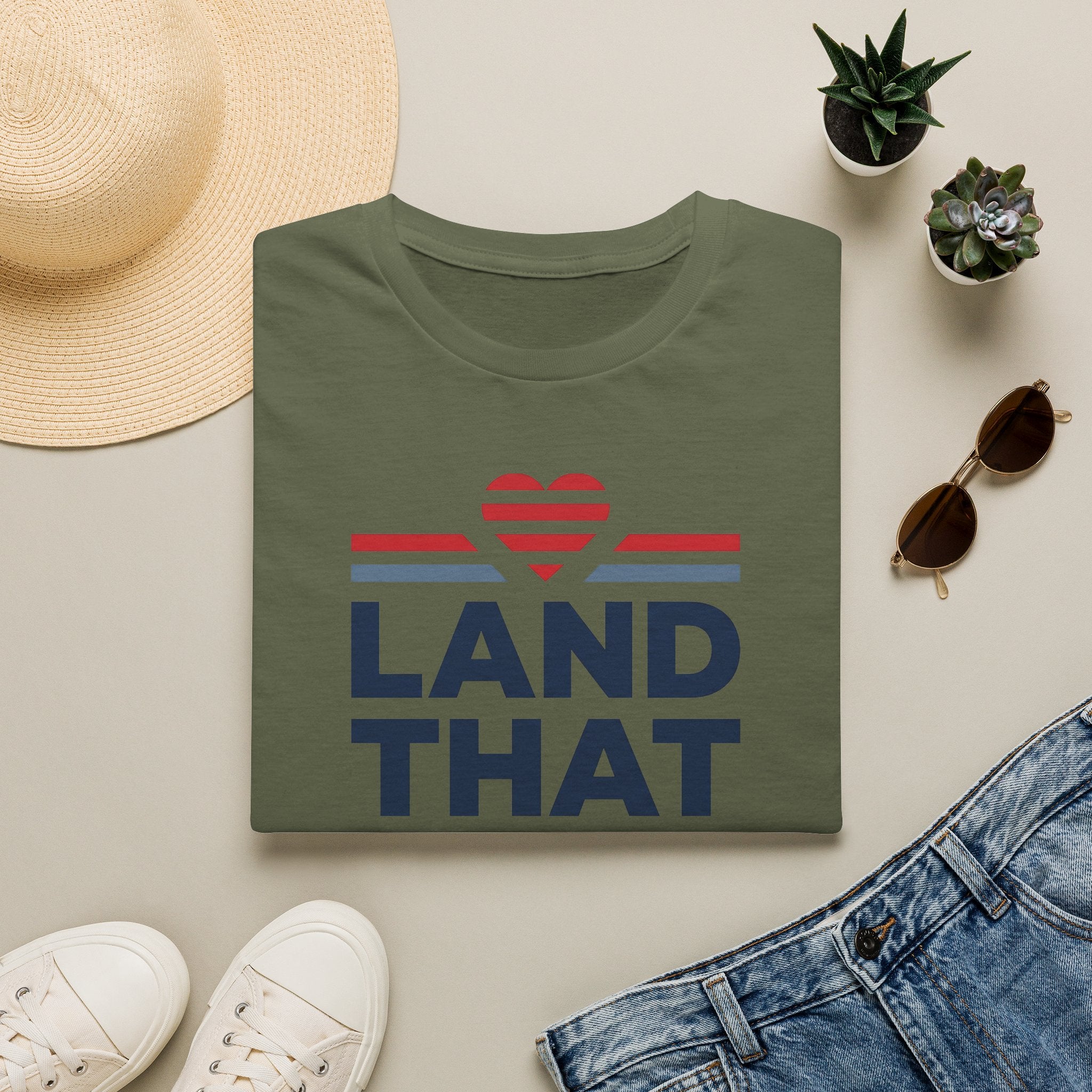 Olive green T-shirt with “LAND THAT” graphic and red heart above blue stripes, crew neck.