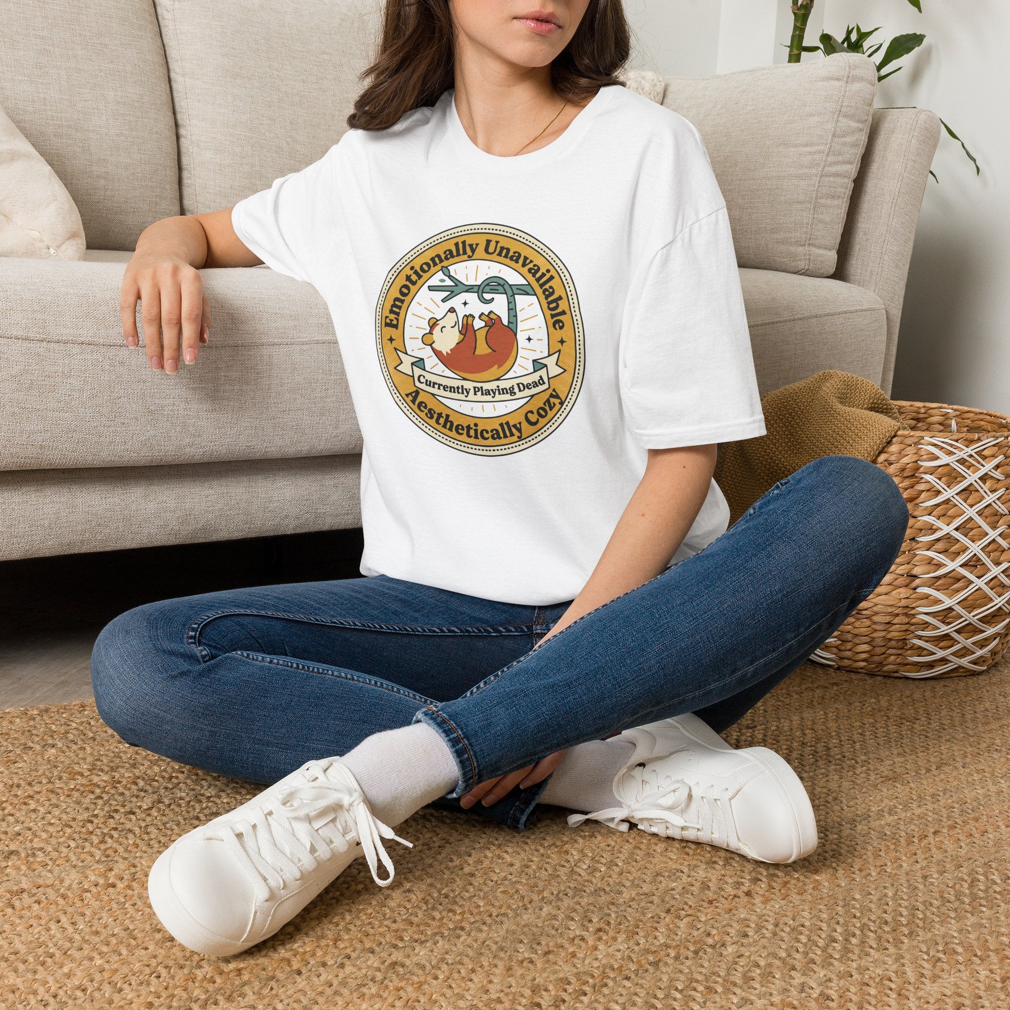 White T-shirt with round sloth graphic front, worn by model sitting with jeans
