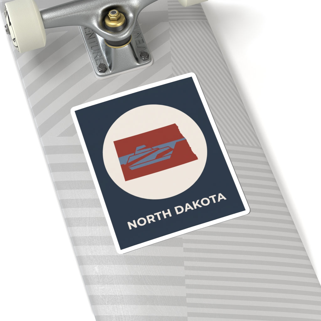 North Dakota map sticker on a notebook, navy square with cream circle and red state graphic