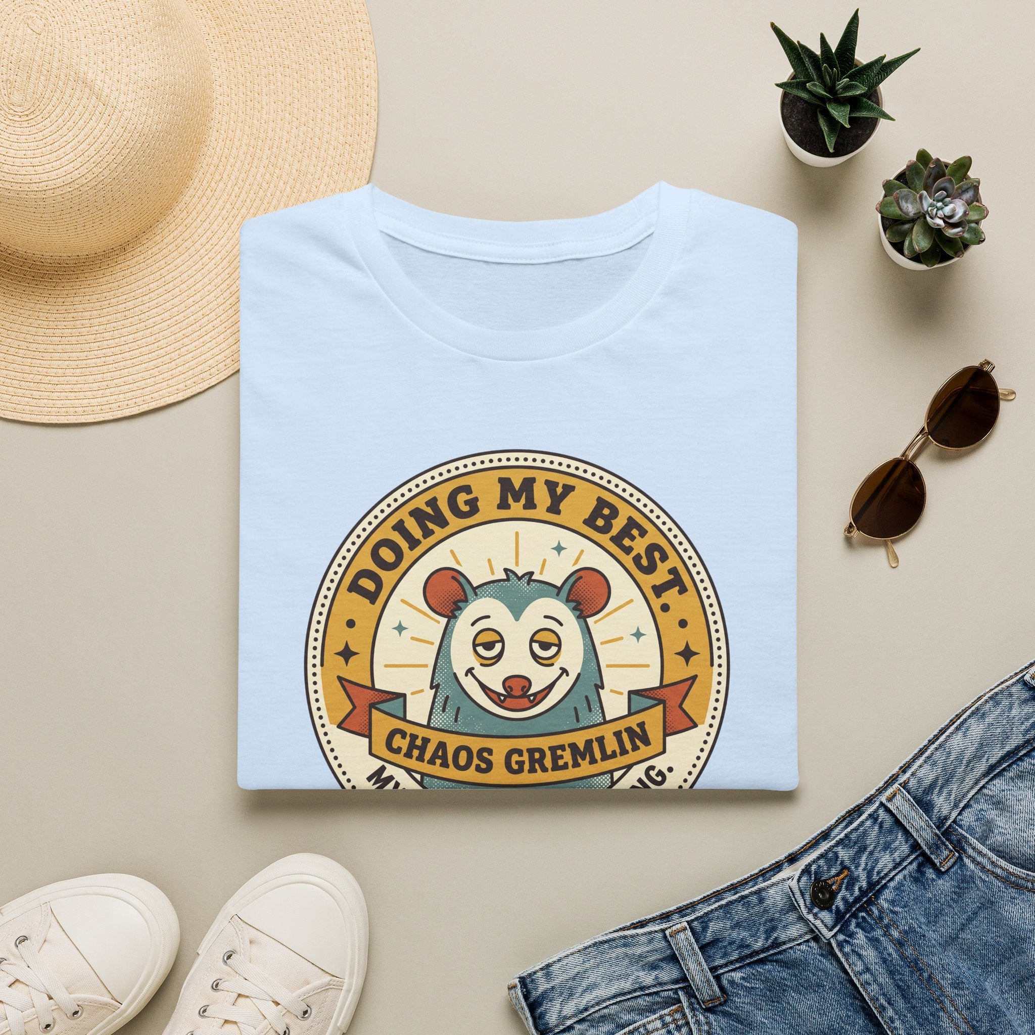 Light blue t-shirt with “Doing My Best Chaos Gremlin” cartoon chest graphic