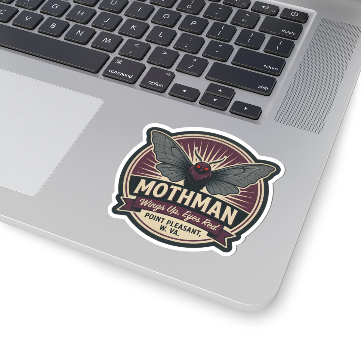 Mothman emblem kiss-cut sticker on laptop lid, round badge with dark wings and red eyes