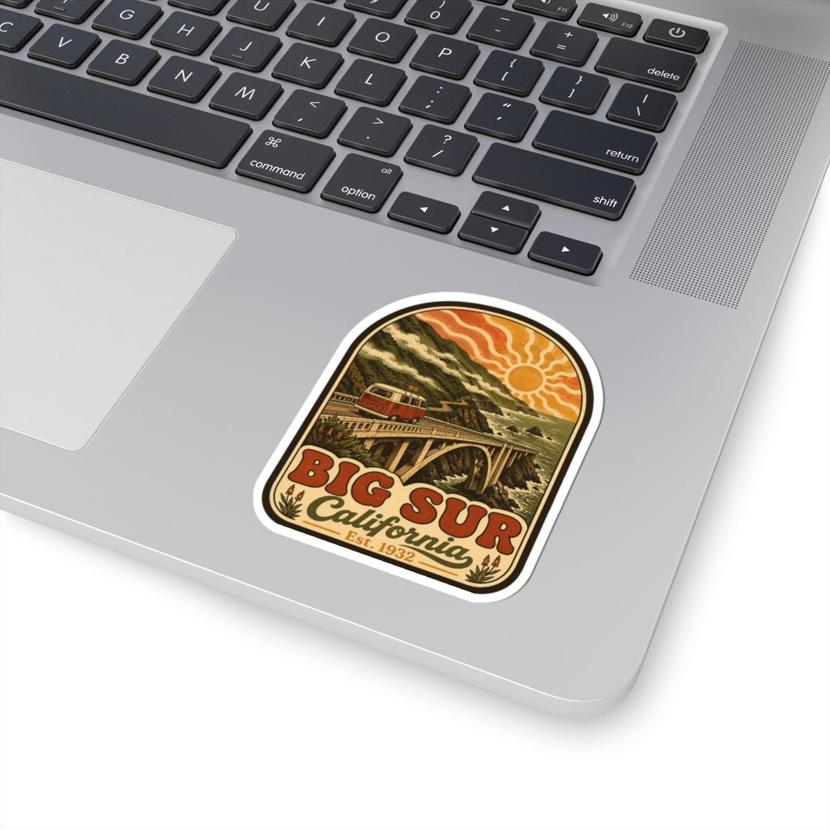 Kiss-cut Big Sur California sticker on laptop keyboard, red camper van and coastal bridge design.