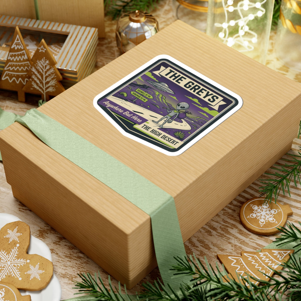 Die-cut sticker on wrapped gift box with alien and UFO over a desert path.