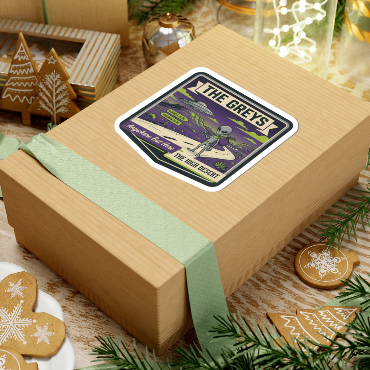 Die-cut sticker on wrapped gift box with alien and UFO over a desert path.
