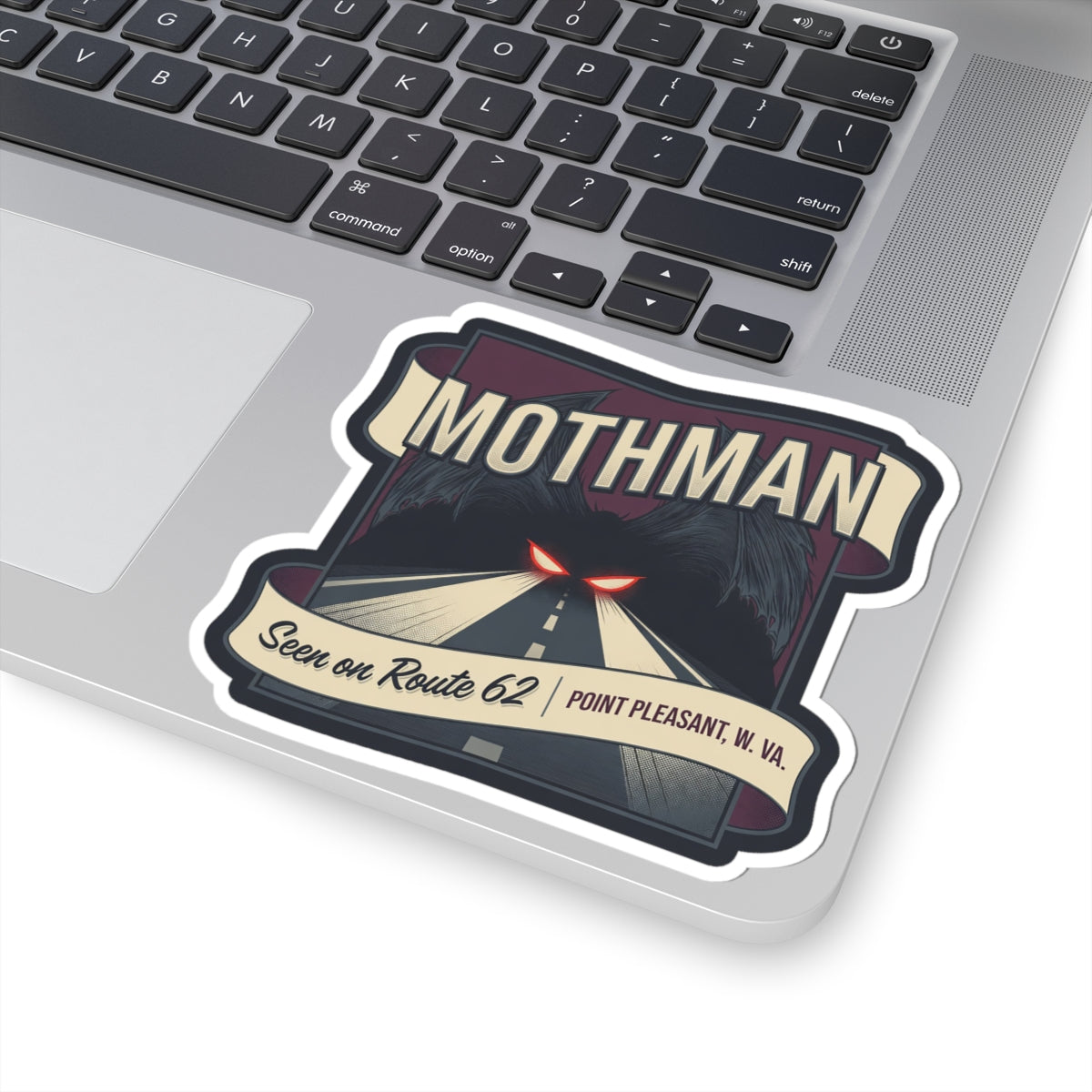 Mothman decal on laptop: road illustration with red glowing eyes, “Seen on Route 62,” and W.Va.