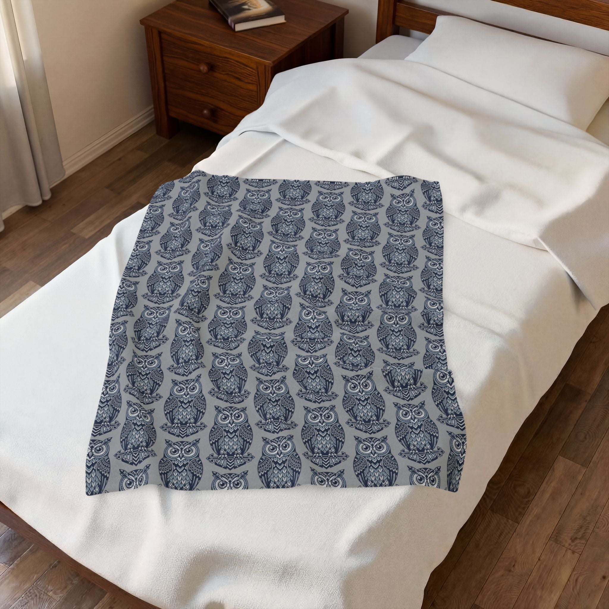 Blue owl-pattern plush blanket folded over bed with repeating owl design