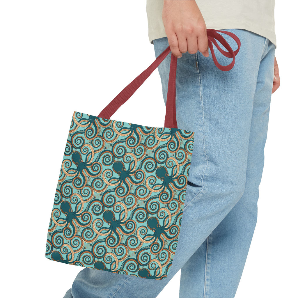 Teal octopus swirl tote bag with red strap, held