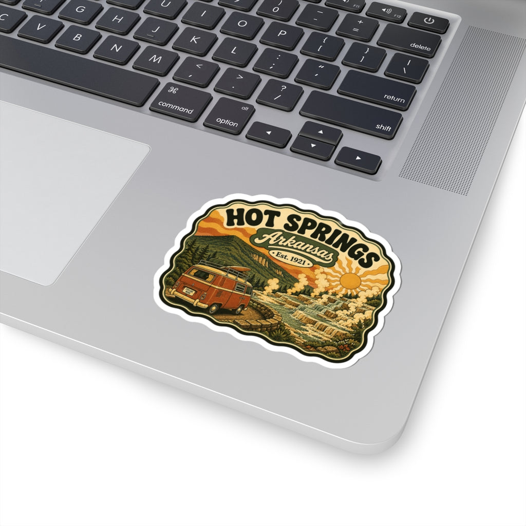 Die-cut Hot Springs Arkansas sticker on laptop lid, featuring a vintage camper van and landscape