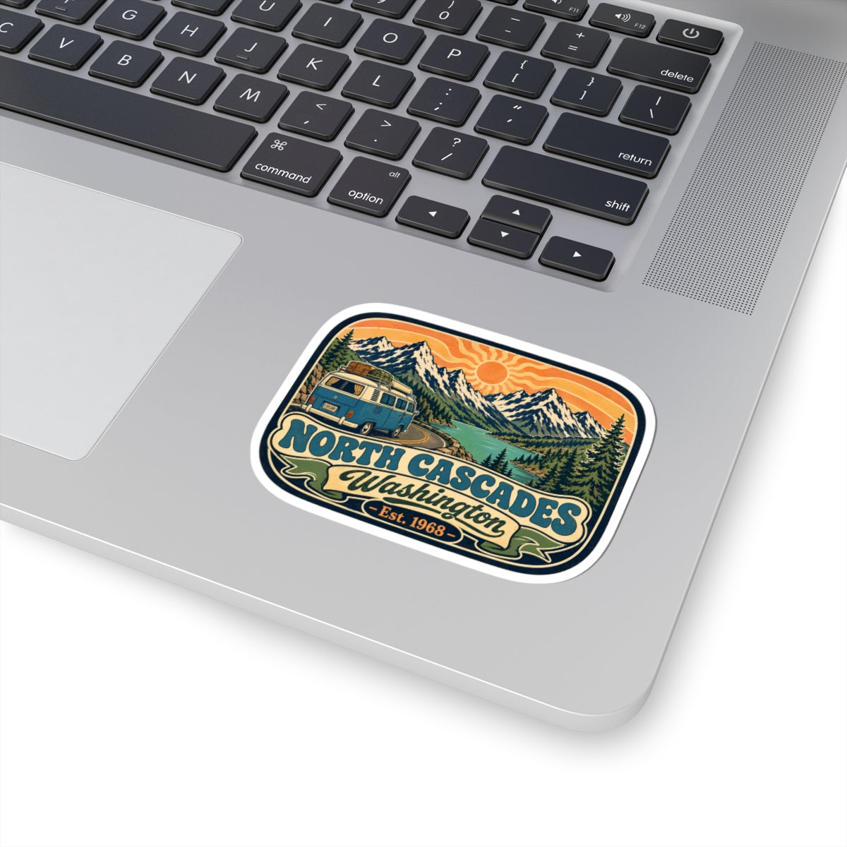 North Cascades sticker on a laptop keyboard, showing camper van, mountains, and sun