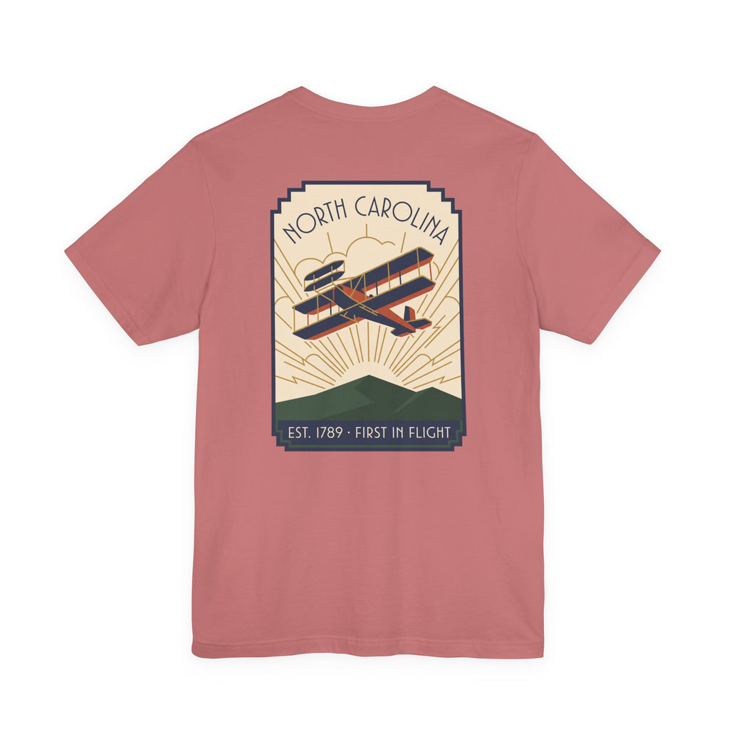 Pinkish red t-shirt with North Carolina biplane graphic and 'Est. 1789 - First in Flight' text