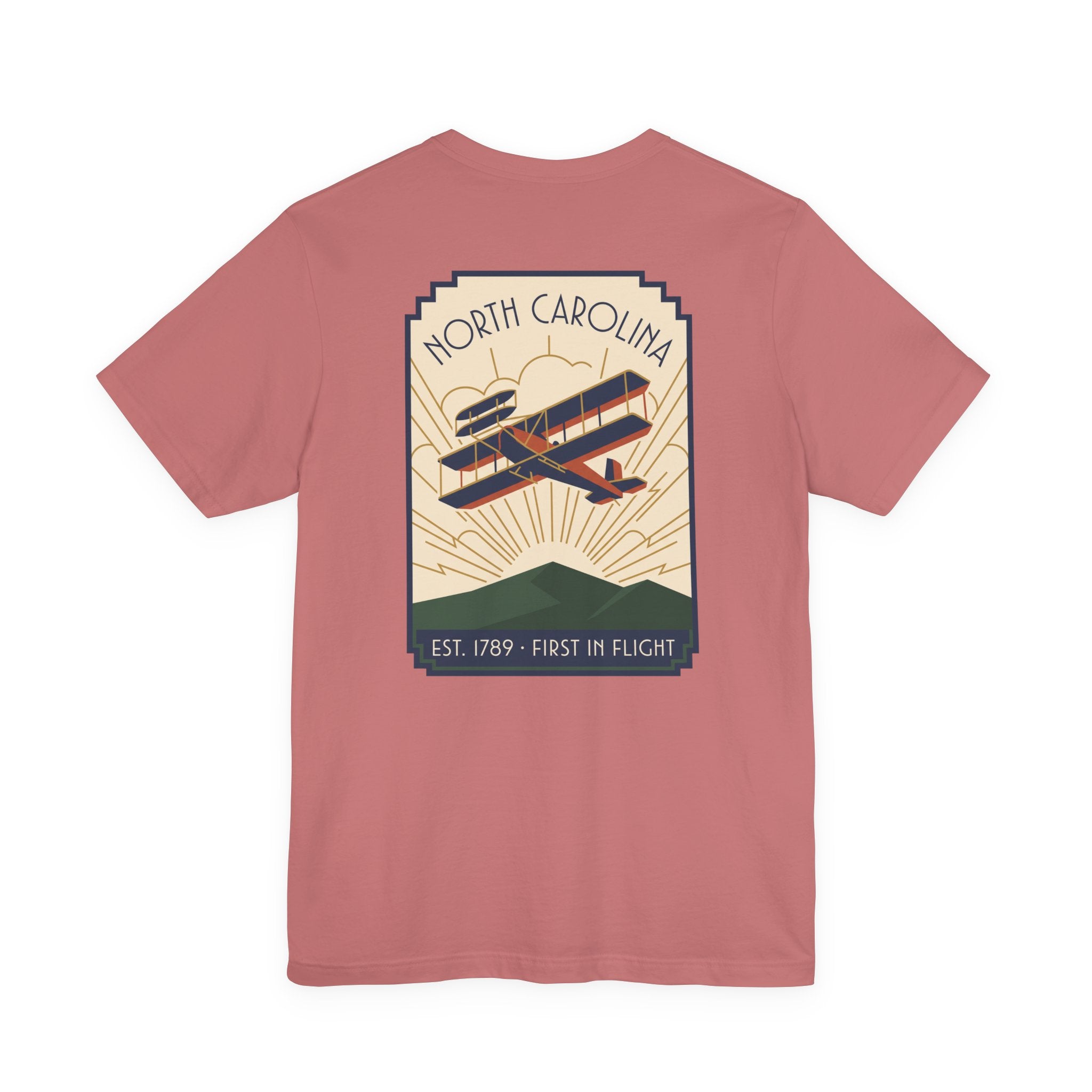 Pinkish red t-shirt with North Carolina biplane graphic and 'Est. 1789 - First in Flight' text