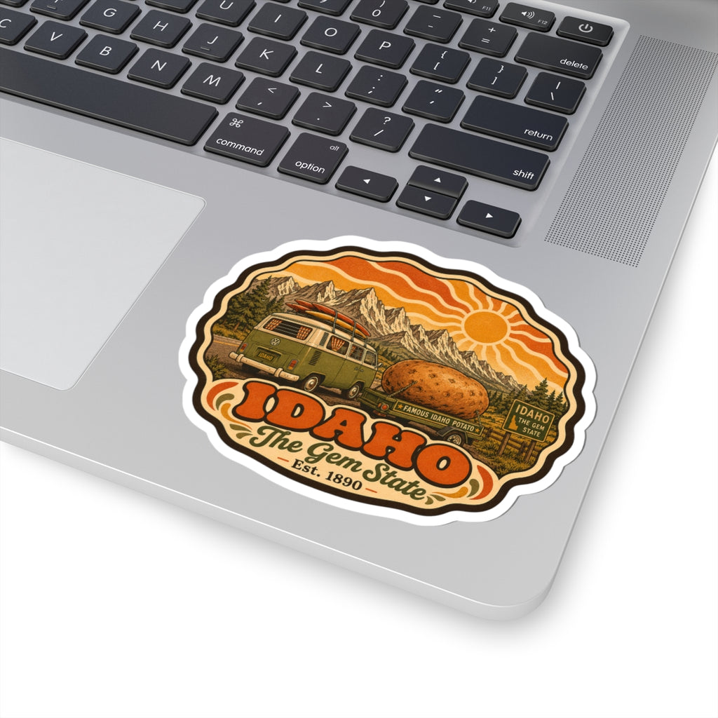 Idaho The Gem State sticker on laptop keyboard, with green van, potato, mountains and orange sun.