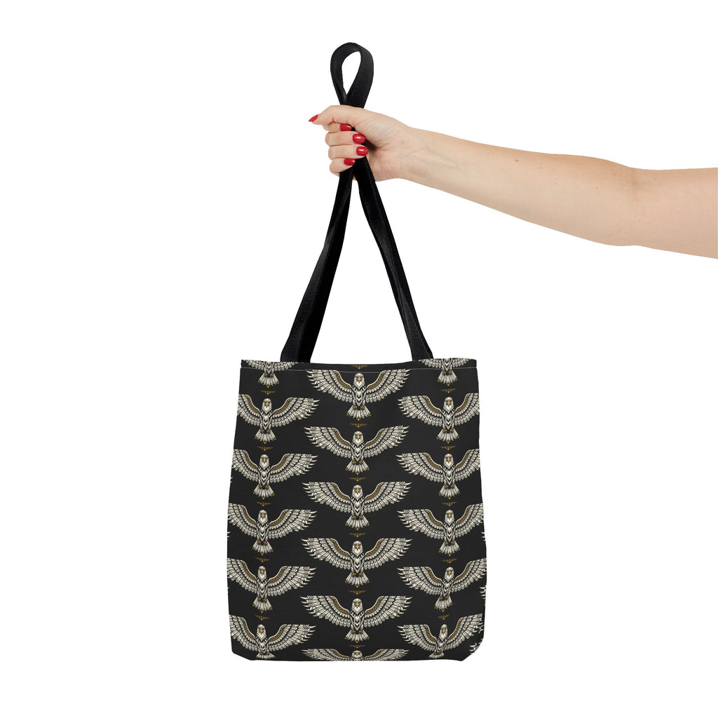 Black tote bag with gold winged scarab pattern and black loop handles, held by hand