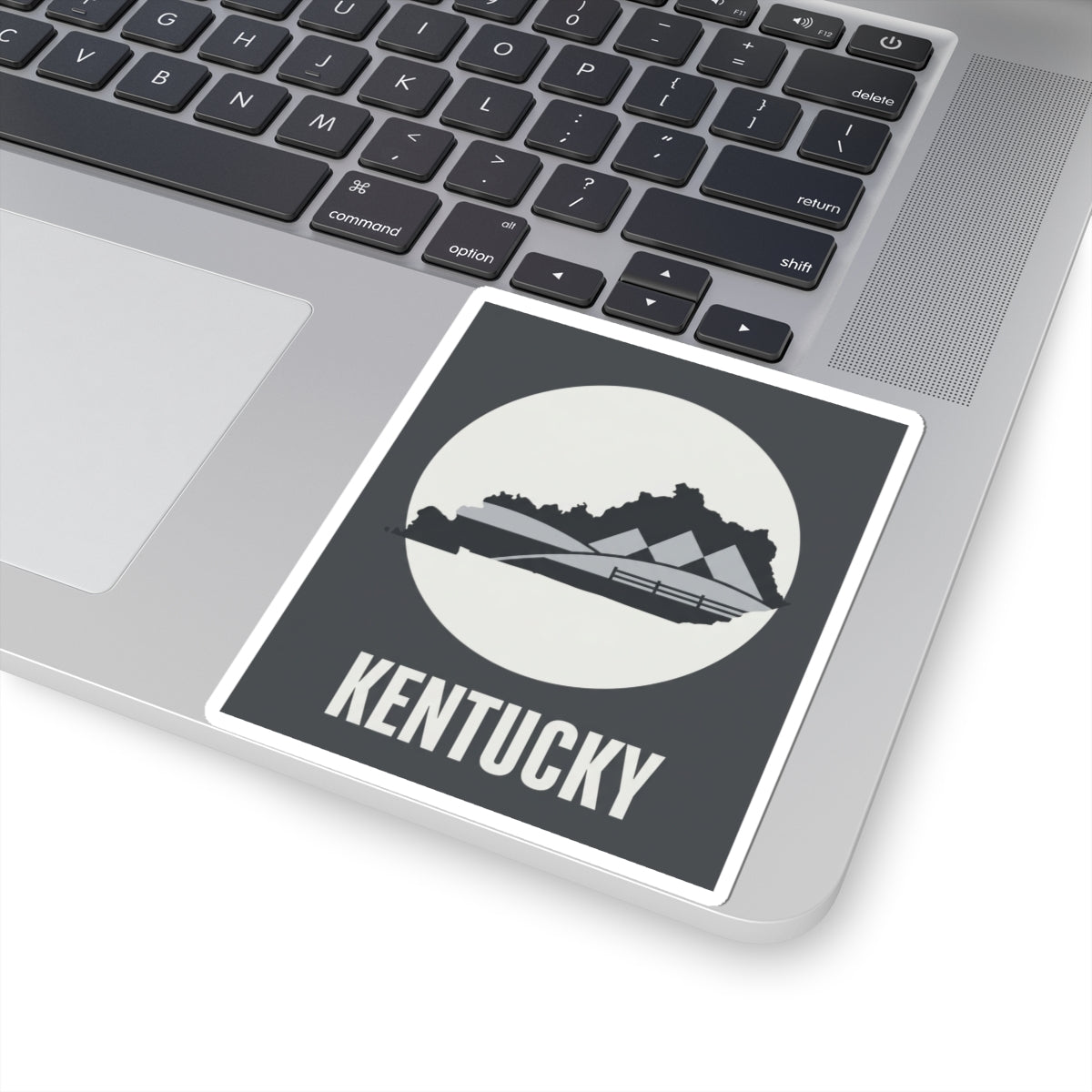 Kentucky vinyl sticker on laptop keyboard, dark gray square with white border and KENTUCKY