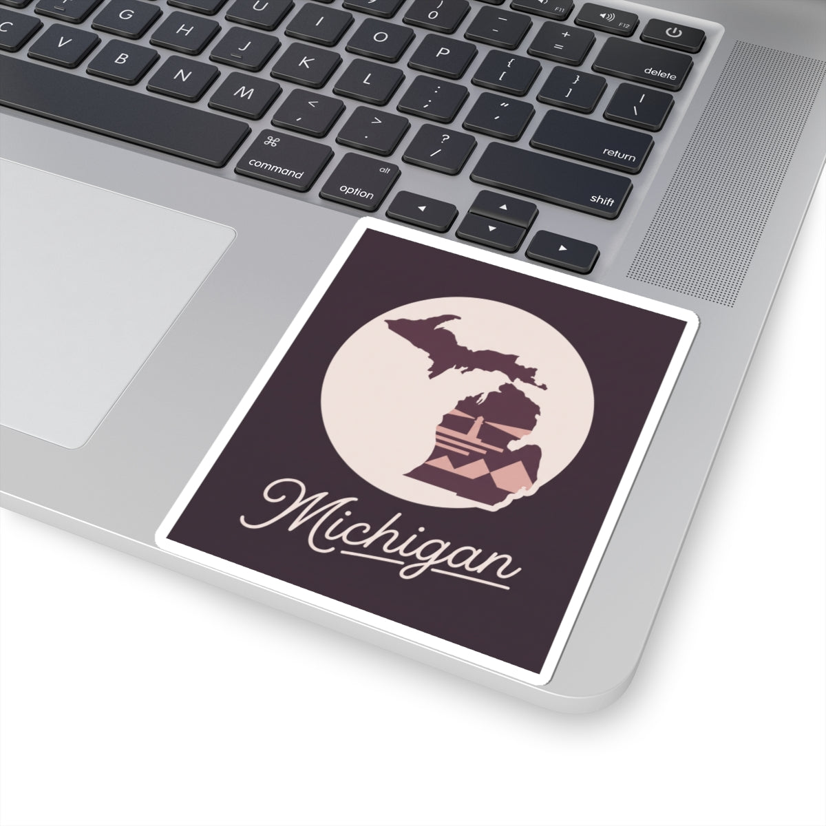 Square Michigan kiss-cut decal on laptop: cream circle with purple lighthouse, “Michigan” in cursive.