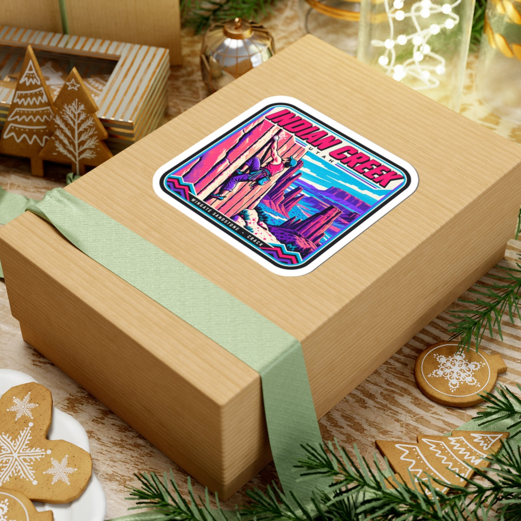 Square “INDIAN CREEK” sticker on a wrapped gift box with ribbon, featuring climber artwork