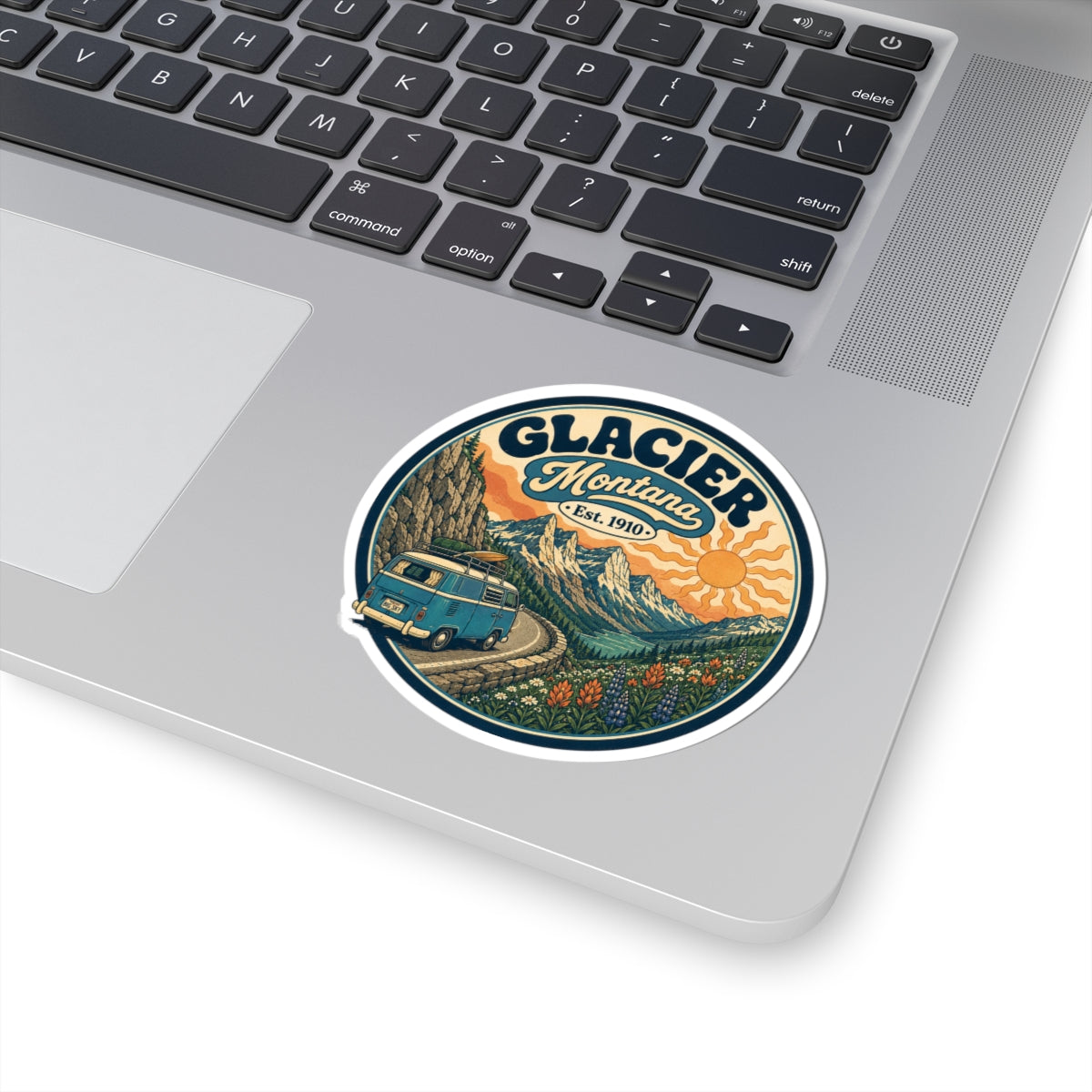 Round kiss-cut sticker with Glacier Montana typography, teal camper van, mountains, and orange sun