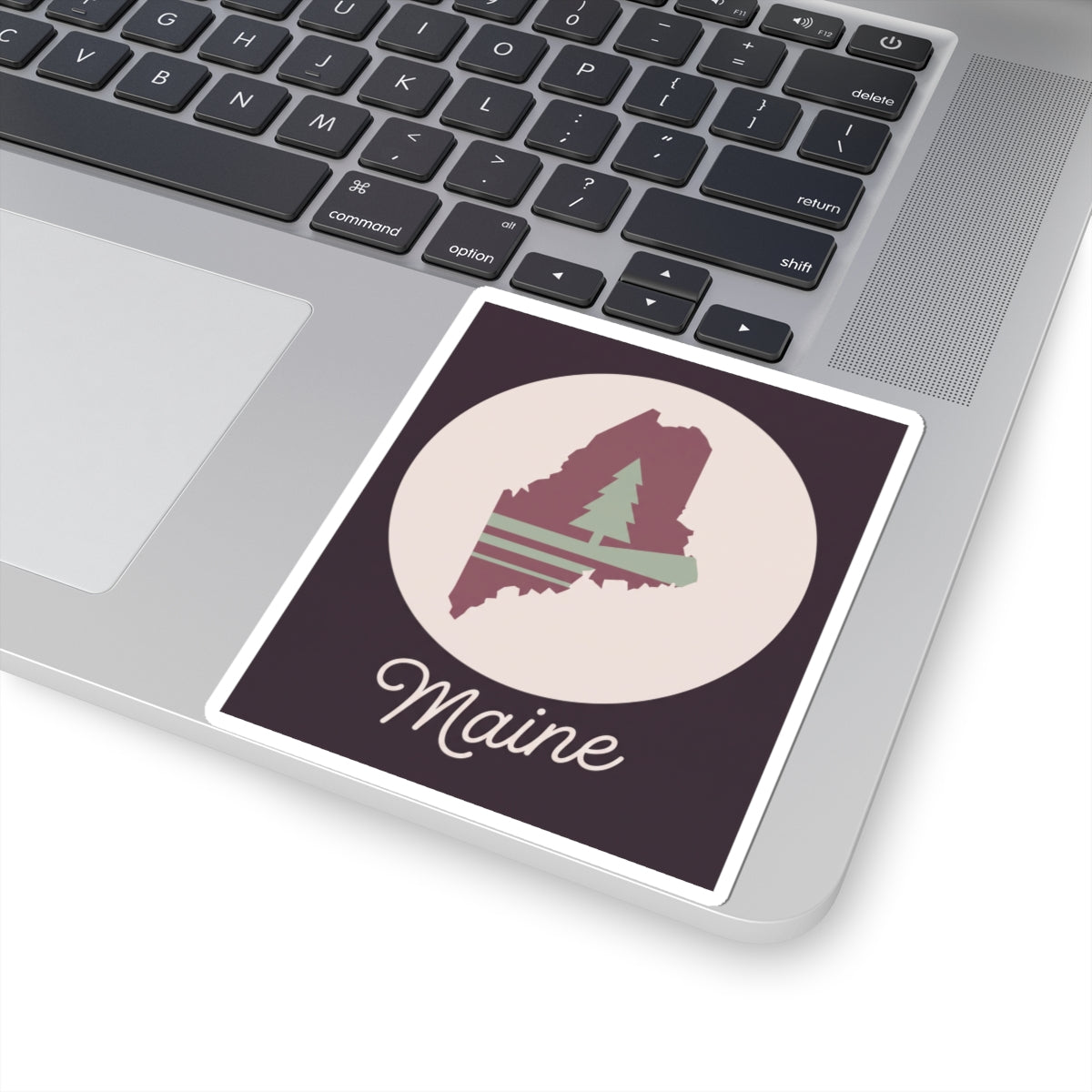 Square Maine silhouette vinyl decal on a laptop, mauve map, pine tree, and 'Maine' lettering.