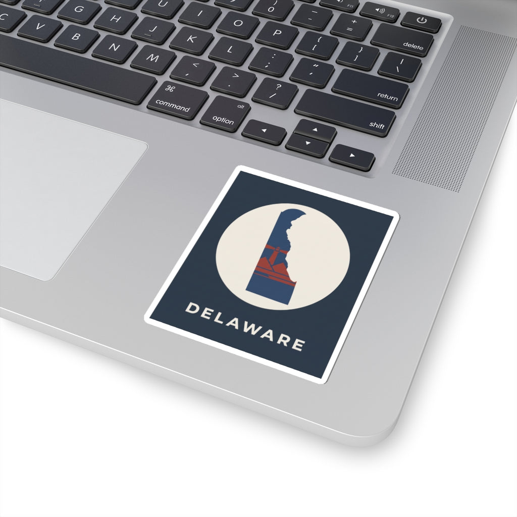 Kiss-cut Delaware sticker on a laptop keyboard, blue/red state design inside white circle