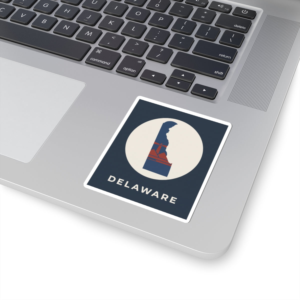 Kiss-cut Delaware sticker on a laptop keyboard, blue/red state design inside white circle