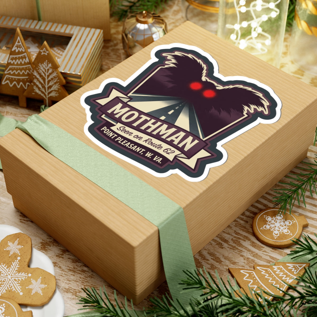 Kiss-cut Mothman sticker on a wrapped gift box, showing red eyes and Route 62 road