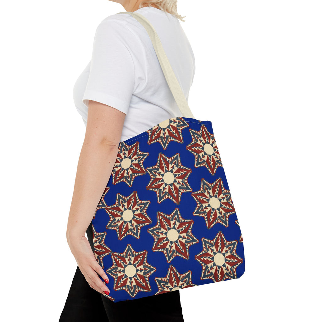 Blue tote bag with starburst floral pattern in cream and red, worn over light straps