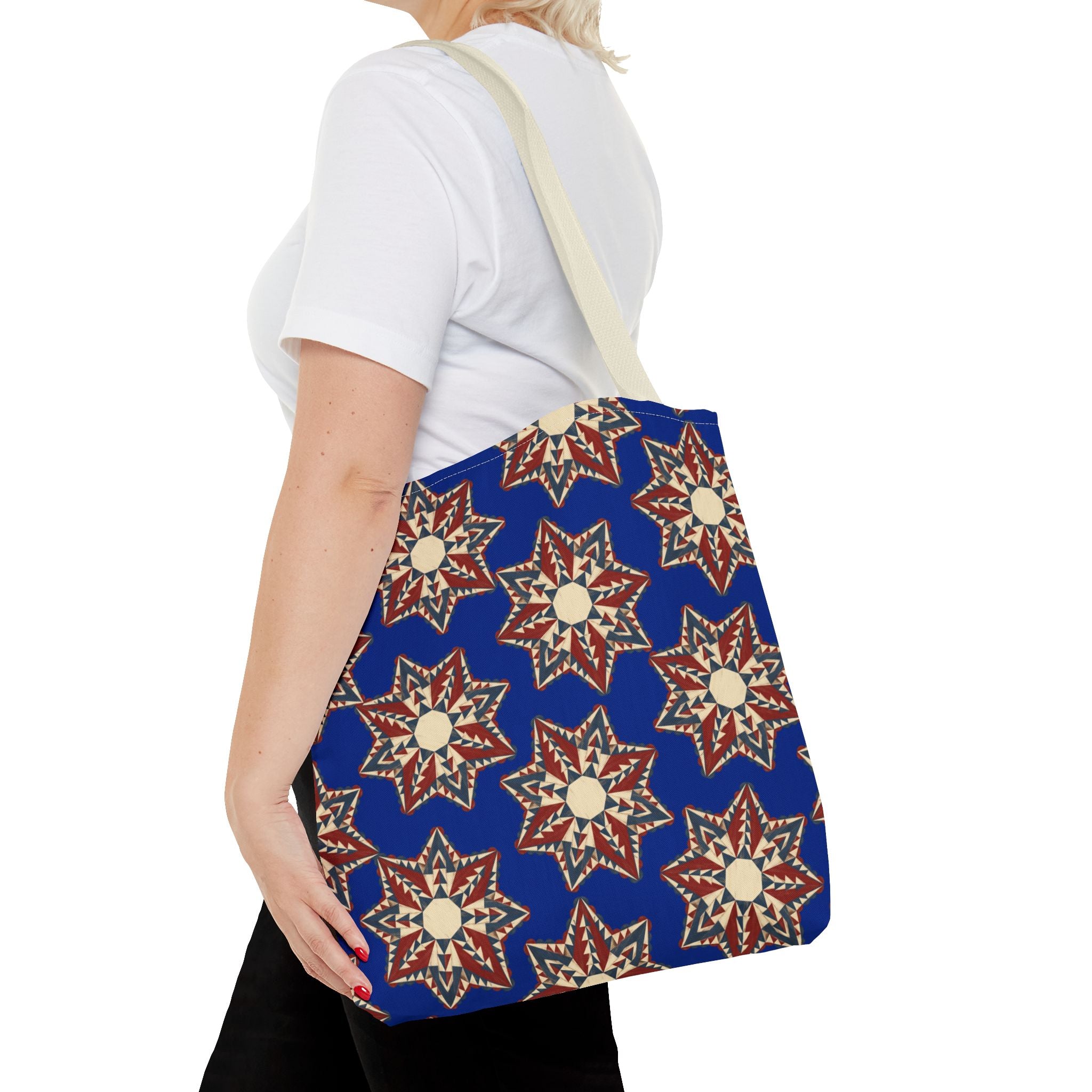 Blue tote bag with starburst floral pattern in cream and red, worn over light straps