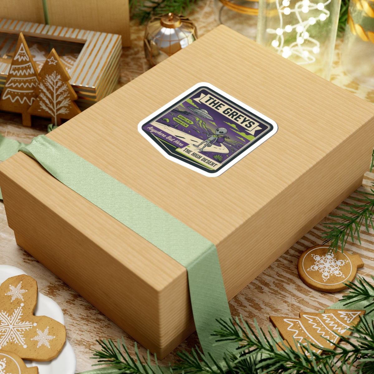 Die-cut sticker on gift box lid with gray alien, UFO, and desert road artwork.