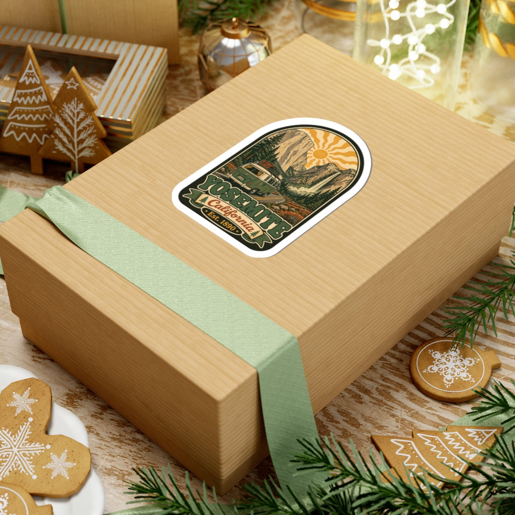 Arched camper van sticker on a gift box ribbon, with mountains, pine trees, and sun