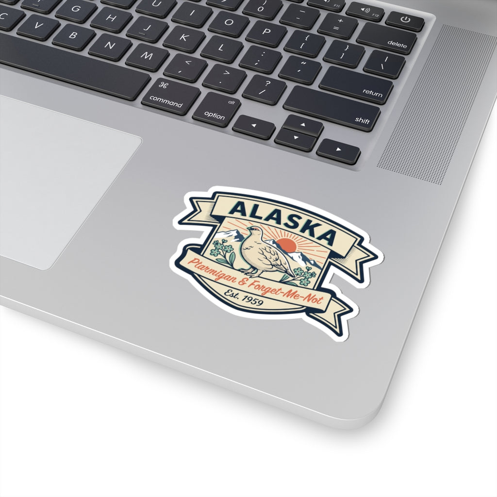 Die-cut Alaska badge sticker on a gray laptop lid with ptarmigan and Est. 1959